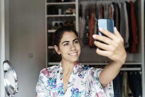 Smiling woman taking selfie on smart phone at home - JMHMF00093