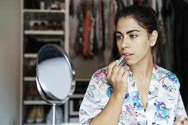 Young female applying lipstick while looking at mirror - JMHMF00096