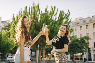 Fröhliche Freundinnen stoßen mit Bierflaschen an, während sie in der Stadt stehen - DCRF00795