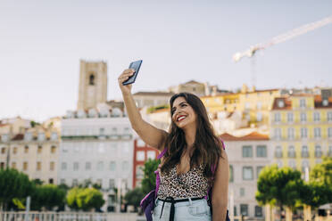 Lächelnde schöne Frau, die ein Selfie mit einem Smartphone macht, während sie in der Stadt steht - DCRF00797