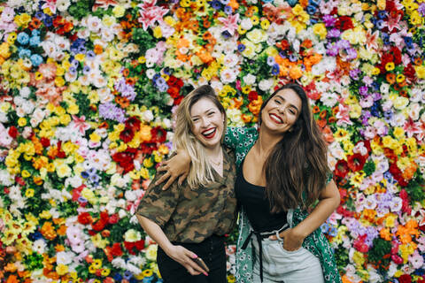 Cheerful beautiful female friends standing against colorful flowers stock photo