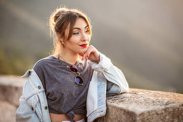 Joyful young woman in trendy casual outfit smiling and looking away on sunny day - ADSF14779