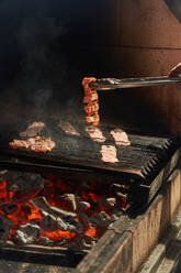 Crop chef turning straps of grilling juicy bacon while cooking with smoke on rack in garden - ADSF14813
