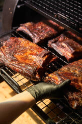 Erntekoch mit Handschuhen beim Grillen von Fleischstücken auf einem Rost im Grill - ADSF14815