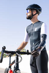 Male amputee cyclist with bicycle standing against clear sky during sunny day - JCMF01224