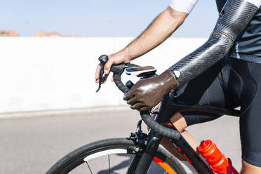 Close-up of male amputee athlete with artificial hand riding bicycle on road - JCMF01227