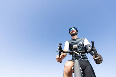 Male amputee cyclist with artificial limb riding bicycle against clear sky - JCMF01232