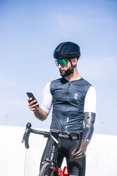 Male amputee cyclist using smart phone while standing with bicycle against clear sky - JCMF01237