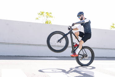 Männlicher Sportler mit Beinprothese bei einem Stunt mit dem Fahrrad auf der Straße gegen den klaren Himmel - JCMF01250
