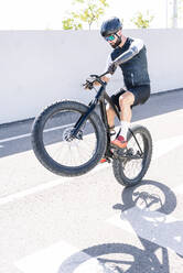 Male amputee athlete performing stunt with bicycle on road during sunny day - JCMF01251