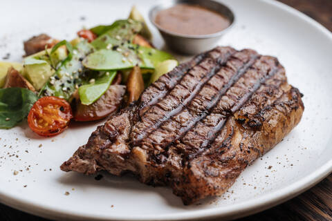 From above closeup of grilled beef steak with basil and vegetable serving on plate with BBQ sauce stock photo