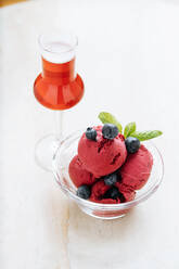 Von oben lilafarbene Eiskugeln in einer Glasschale, dekoriert mit frischen Blaubeeren und Minze und serviert mit einem Glas eines roten Getränks im Restaurant - ADSF14840