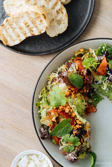 Draufsicht auf einen leckeren Salat mit gekochtem Tintenfisch und getrockneten Tomaten, elegant dekoriert mit Grünzeug auf einem halben Teller und serviert mit geröstetem Brot - ADSF14847