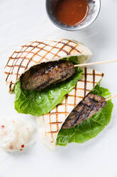 Fresh lettuce leaf and minced meat kebab wrapped in grilled tortilla and placed near cup with spicy sauce on cafe table - ADSF14856