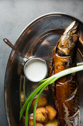 Draufsicht auf leckeren gebratenen Fisch und Kartoffeln, serviert mit reifer Schalotte und Sahnesauce auf einem Metallteller im Restaurant - ADSF14859