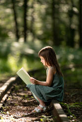 Seitenansicht eines jungen Mädchens, das im Wald sitzt und eine interessante Geschichte liest - ADSF14865