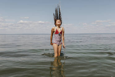 Spiegelung eines Mädchens mit zerzaustem Haar, das am Strand im Wasser steht - OGF00495