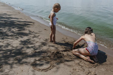 Young girls playing in sand during summer vacation at beach - OGF00498