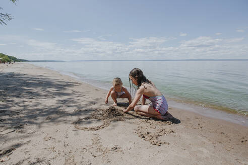 Schwestern spielen im Sand im Sommer am Strand an einem sonnigen Tag - OGF00499