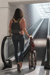 Junge Frau mit Koffer, die sich auf den Gehweg eines Flughafens bewegt - MTBF00656