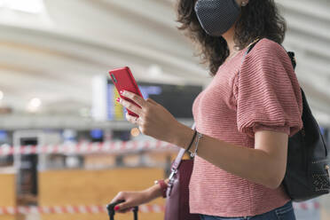 Close-up of woman with protective mask on face using smart phone while standing at airport - MTBF00658