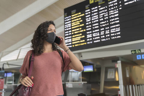 Young woman with protective face mask talking on smart phone while standing at airport stock photo