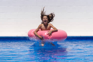 Aufgeregtes Mädchen mit rosa aufblasbarem Ring genießt Sommertag im Schwimmbad während der Ferien - ADSF14890