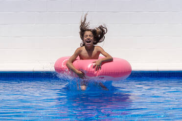 Excited girl with pink inflatable ring enjoying summer day in swimming pool during holidays - ADSF14890