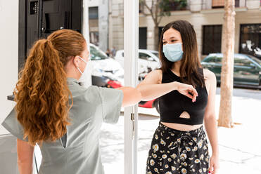 Professional staff in uniform and protective mask greeting female patient with gesture in entrance of modern spa salon during coronavirus pandemic - ADSF14905