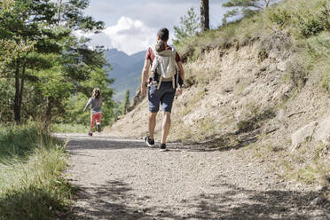 Father hiking with his children, carrying son on back while daughter is running - JCZF00212