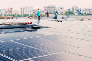 Gesellschaft ethnischer männlicher Arbeiter bei der Installation moderner Solarzellen auf der Baustelle einer Fabrik - ADSF14918