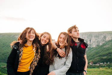 Gruppe von glücklichen Freunden, die sich vor dem Hintergrund einer spektakulären Berglandschaft in Siebenbürgen umarmen und fröhlich in die Kamera schauen - ADSF14946