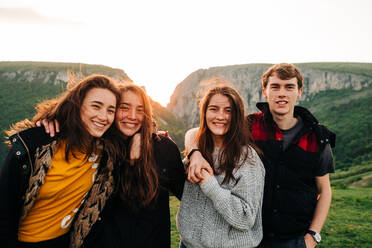 Gruppe von glücklichen Freunden, die sich vor dem Hintergrund einer spektakulären Berglandschaft in Siebenbürgen umarmen und fröhlich in die Kamera schauen - ADSF14947