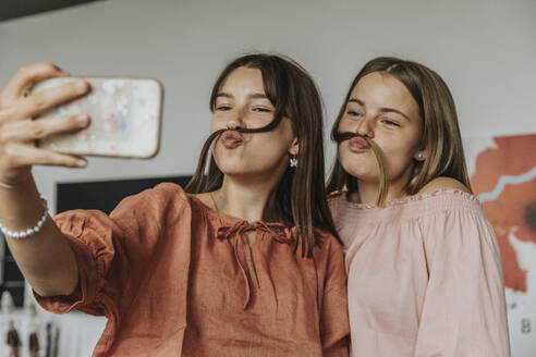 Friends making fake mustache with hair while taking selfie at home - MFF06091