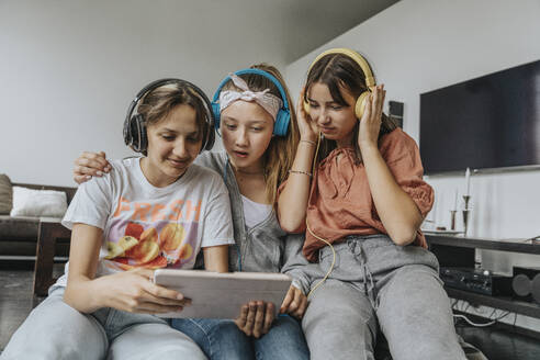Freunde im Teenageralter hören Musik über Kopfhörer, während sie zu Hause ein digitales Tablet benutzen - MFF06092