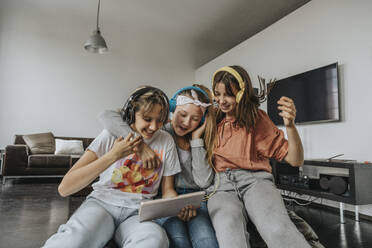 Fröhliche Freunde hören Musik über Kopfhörer, während sie zu Hause ein digitales Tablet benutzen - MFF06093