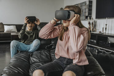 Friends looking through virtual reality simulators while sitting on couch at home - MFF06094