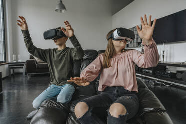 Friends looking through virtual reality simulators while relaxing on couch at home - MFF06095