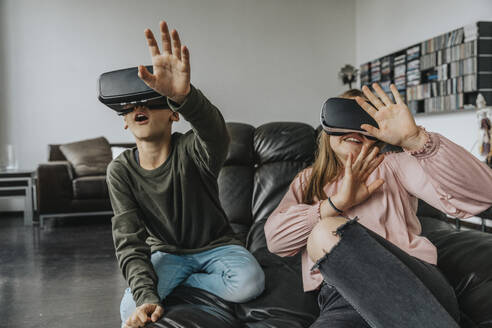 Fröhliche Freunde, die zu Hause auf der Couch sitzen und durch Virtual-Reality-Simulatoren schauen - MFF06097
