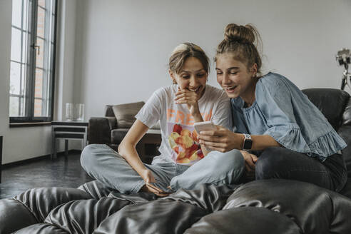 Fröhliche Freunde benutzen ein Smartphone, während sie sich zu Hause auf der Couch entspannen - MFF06100