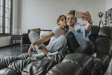Friends taking selfie with smart phone while sitting on couch at home - MFF06101