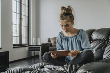 Mädchen, das ein digitales Tablet benutzt, während es sich auf dem Sofa zu Hause entspannt - MFF06103