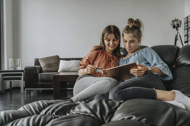 Freunde beim Online-Shopping über ein digitales Tablet, während sie sich zu Hause auf dem Sofa entspannen - MFF06106
