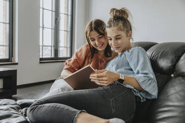 Friends using digital tablet while relaxing on sofa at home - MFF06107