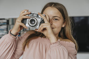 Nahaufnahme eines Mädchens, das mit einer alten Kamera zu Hause fotografiert - MFF06110