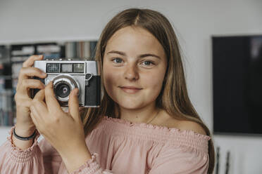 Nahaufnahme eines Mädchens, das eine alte Kamera zu Hause hält - MFF06111