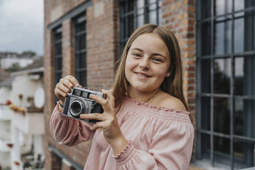 Close-up of smiling girl with old camera standing outside house - MFF06112