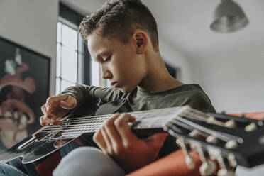 Nahaufnahme eines Jungen, der zu Hause sitzt und Gitarre spielt - MFF06115