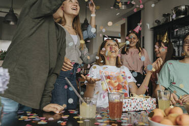 Friends throwing confetti on cheerful teenage girl in birthday party at home - MFF06123