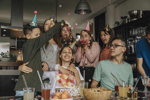 Glückliche Freunde werfen Konfetti auf Teenager-Mädchen in Geburtstagsparty zu Hause - MFF06124